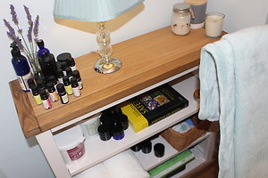 A wooden shelf in the cabin: lavender in a jar, a lamp, candles, a row of small dark essential-oil bottles and a folded towel.